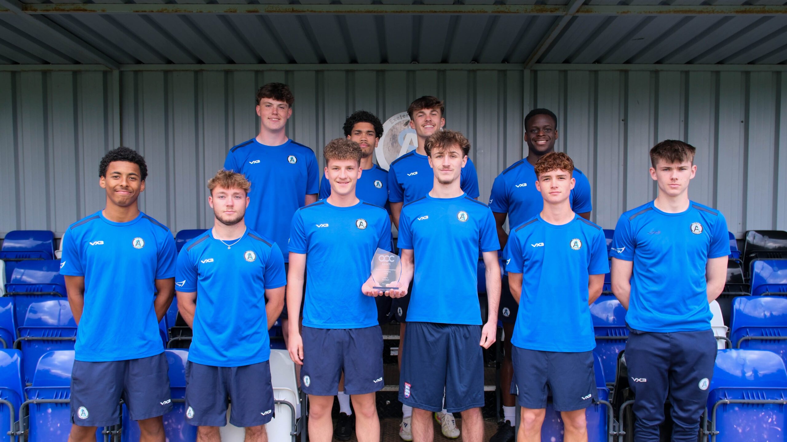 Ten Exeter College football players hold up a trophy 