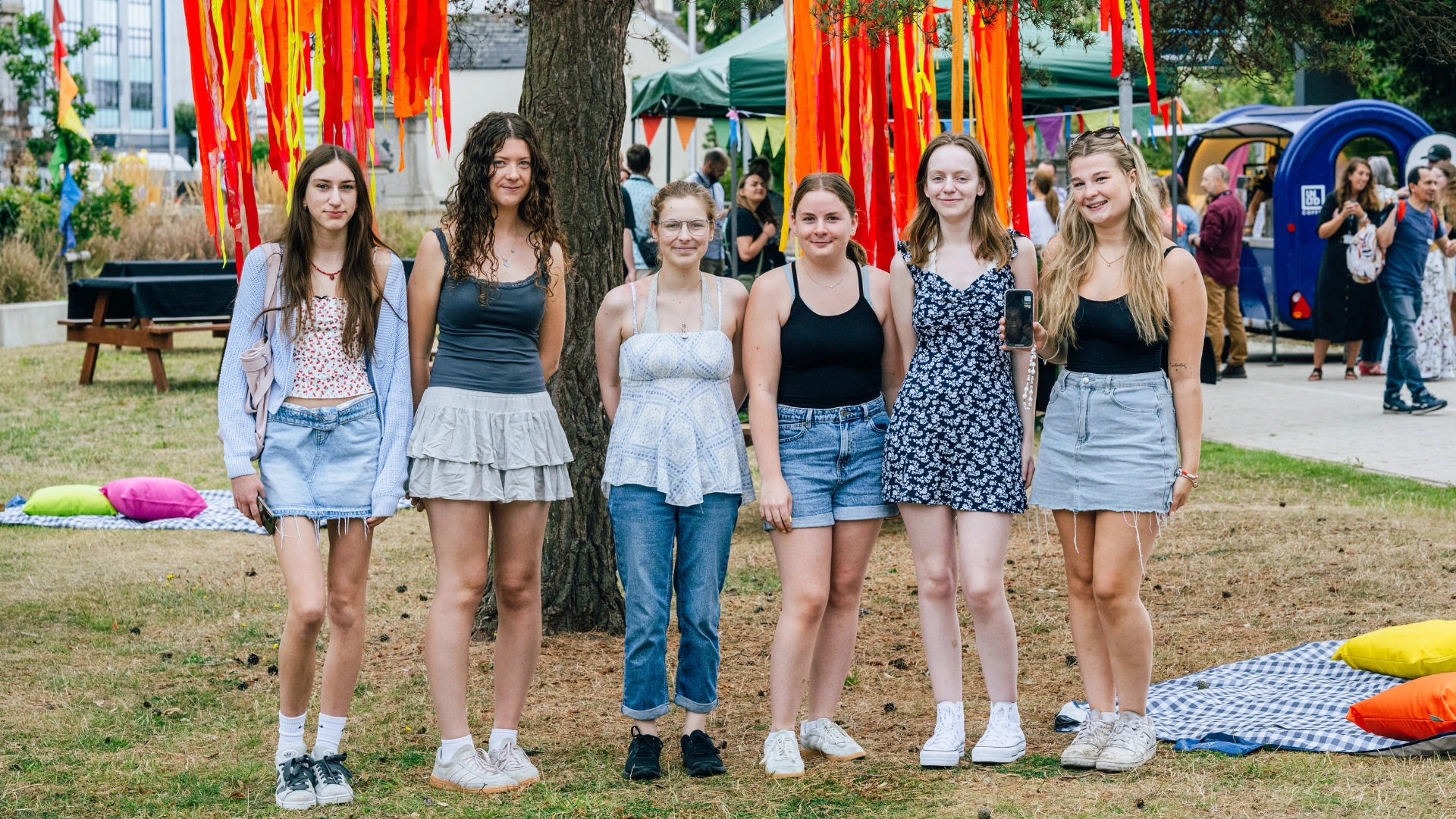 A group of students standing together outdoors at Results Day, with colourful ribbons hanging from trees behind them.