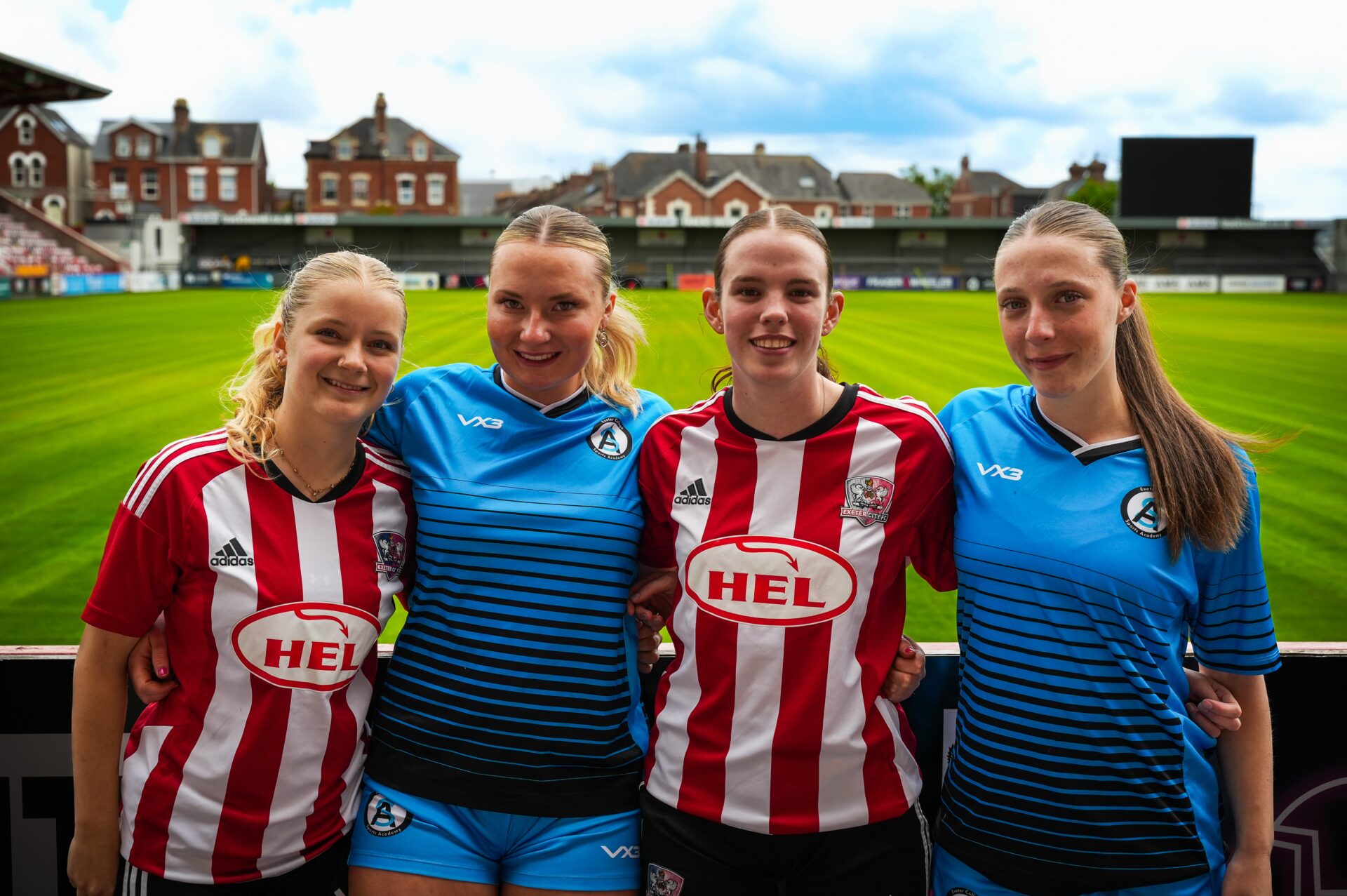 Four academy footballers standing in front of a pitch in a football stadium. 